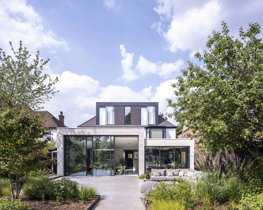 Rear façade of No Ordinary House with a glazed extension opening onto the garden